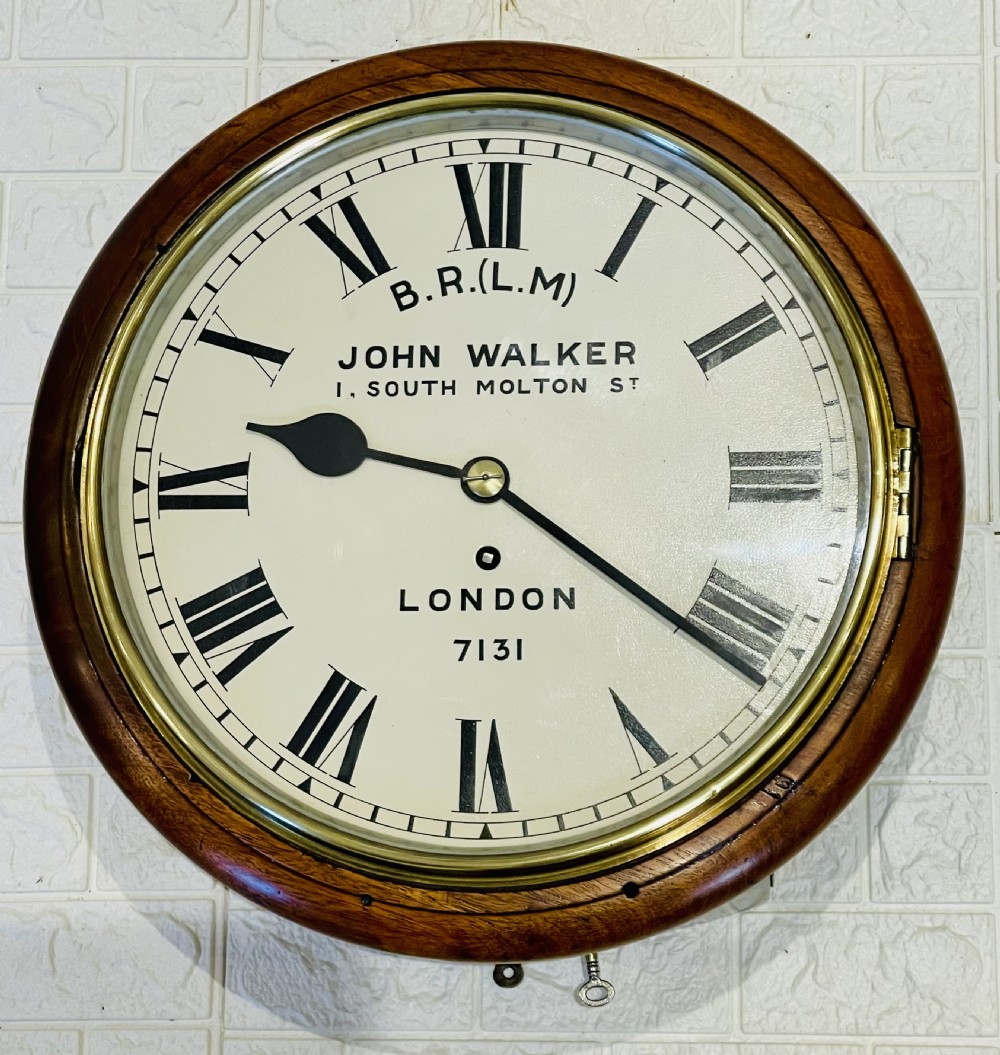 A circular mahogany framed fusee wall clock featuring a cream painted dial with Roman numerals, a brass hinged bezel, and British Rail London Midland markings.