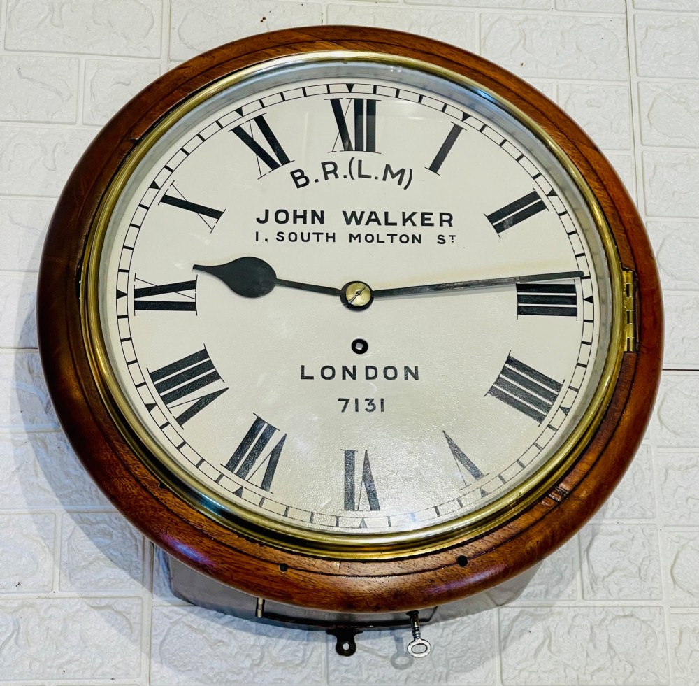 A circular mahogany framed fusee wall clock featuring a cream painted dial with Roman numerals, a brass hinged bezel, and British Rail London Midland markings. View V