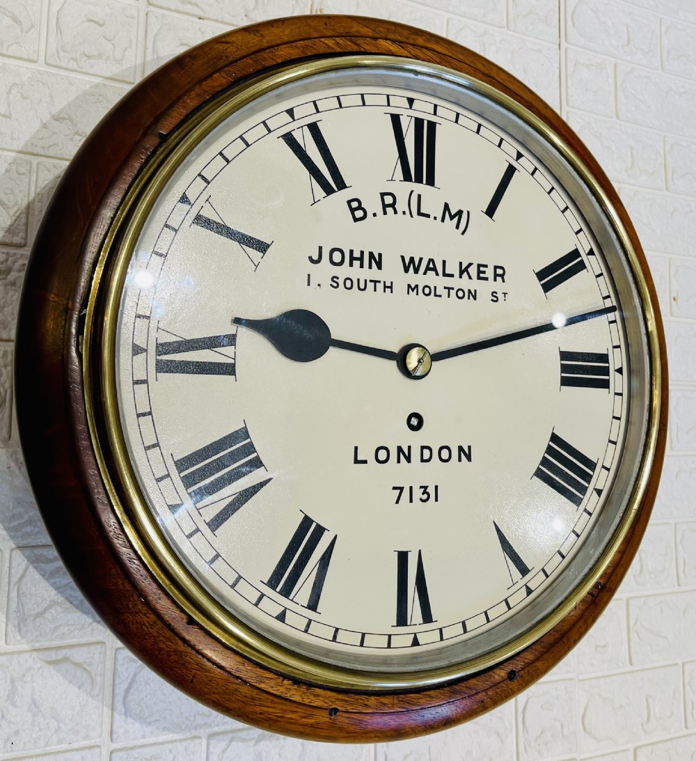 A circular mahogany framed fusee wall clock featuring a cream painted dial with Roman numerals, a brass hinged bezel, and British Rail London Midland markings. View VI