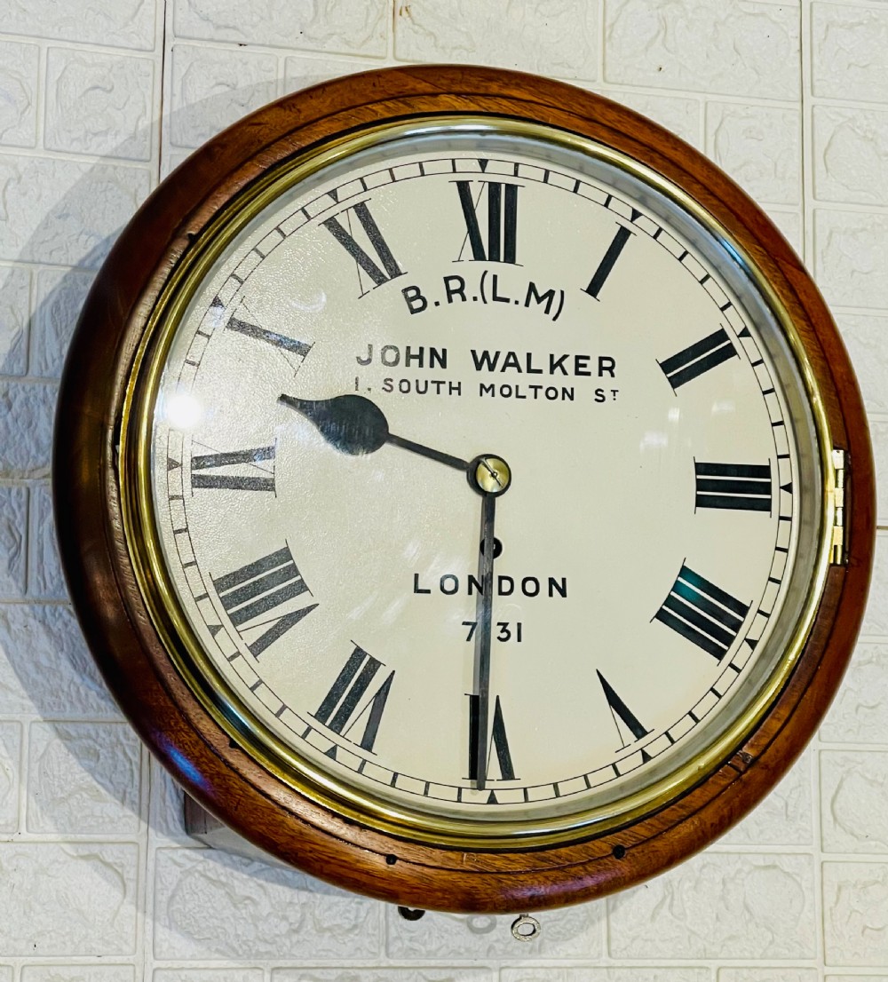 A circular mahogany framed fusee wall clock featuring a cream painted dial with Roman numerals, a brass hinged bezel, and British Rail London Midland markings. View VII