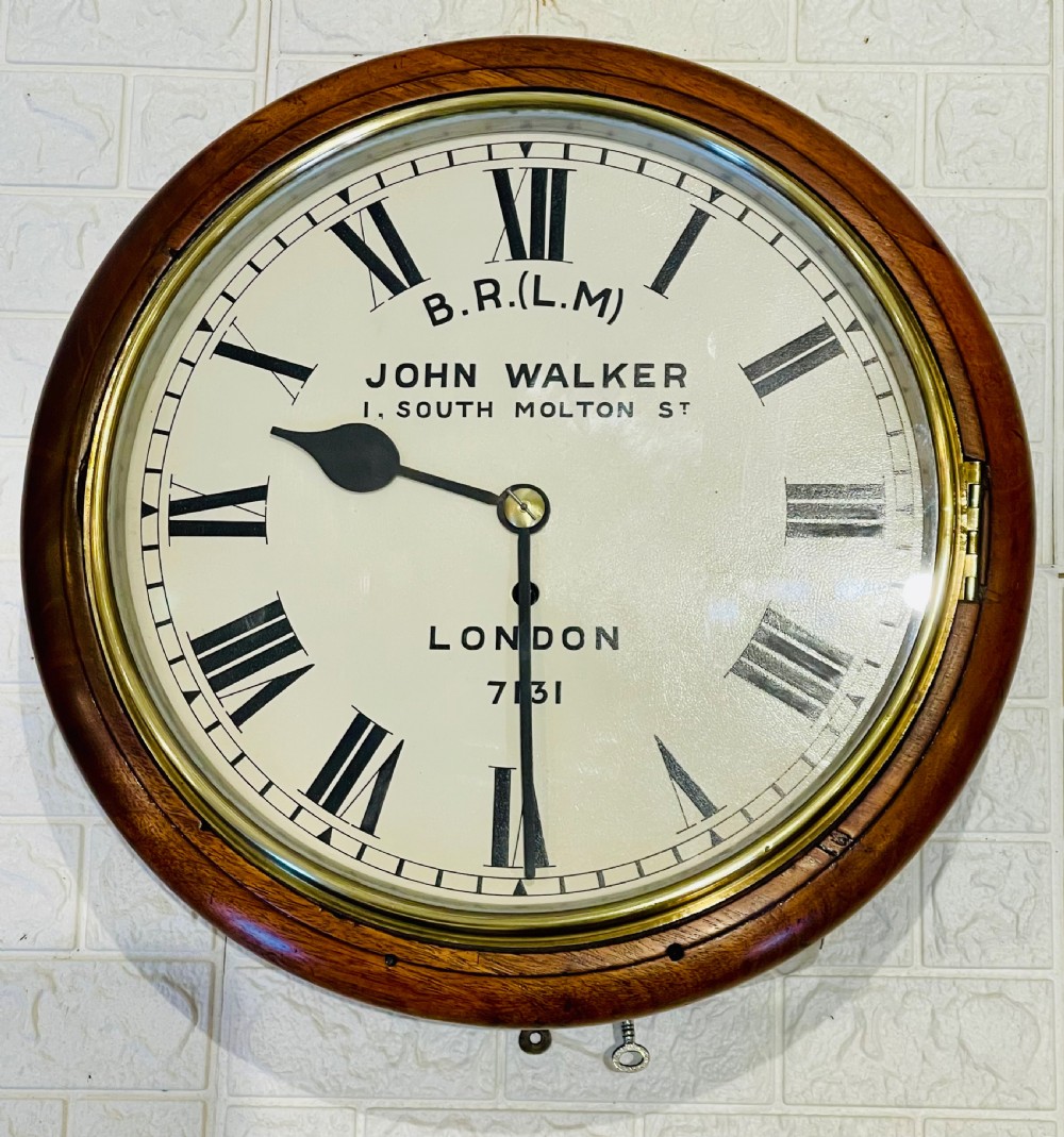 A circular mahogany framed fusee wall clock featuring a cream painted dial with Roman numerals, a brass hinged bezel, and British Rail London Midland markings. View VIII
