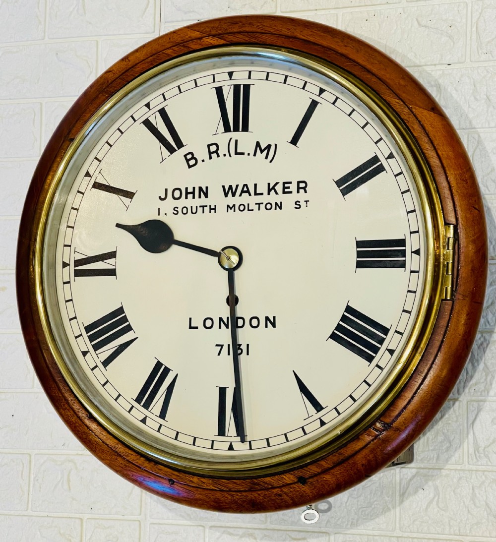 A circular mahogany framed fusee wall clock featuring a cream painted dial with Roman numerals, a brass hinged bezel, and British Rail London Midland markings. View IX