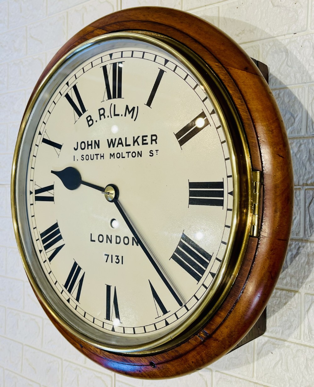 A circular mahogany framed fusee wall clock featuring a cream painted dial with Roman numerals, a brass hinged bezel, and British Rail London Midland markings. View X