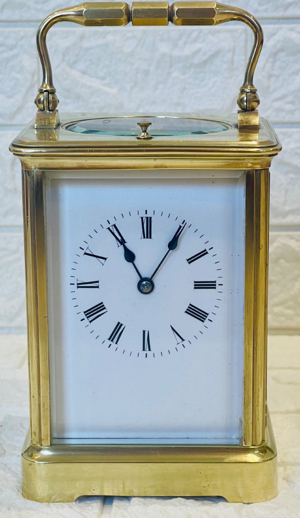 An antique brass carriage clock featuring a rectangular glass case, top carrying handle, and a white enamel dial with black Roman numerals.