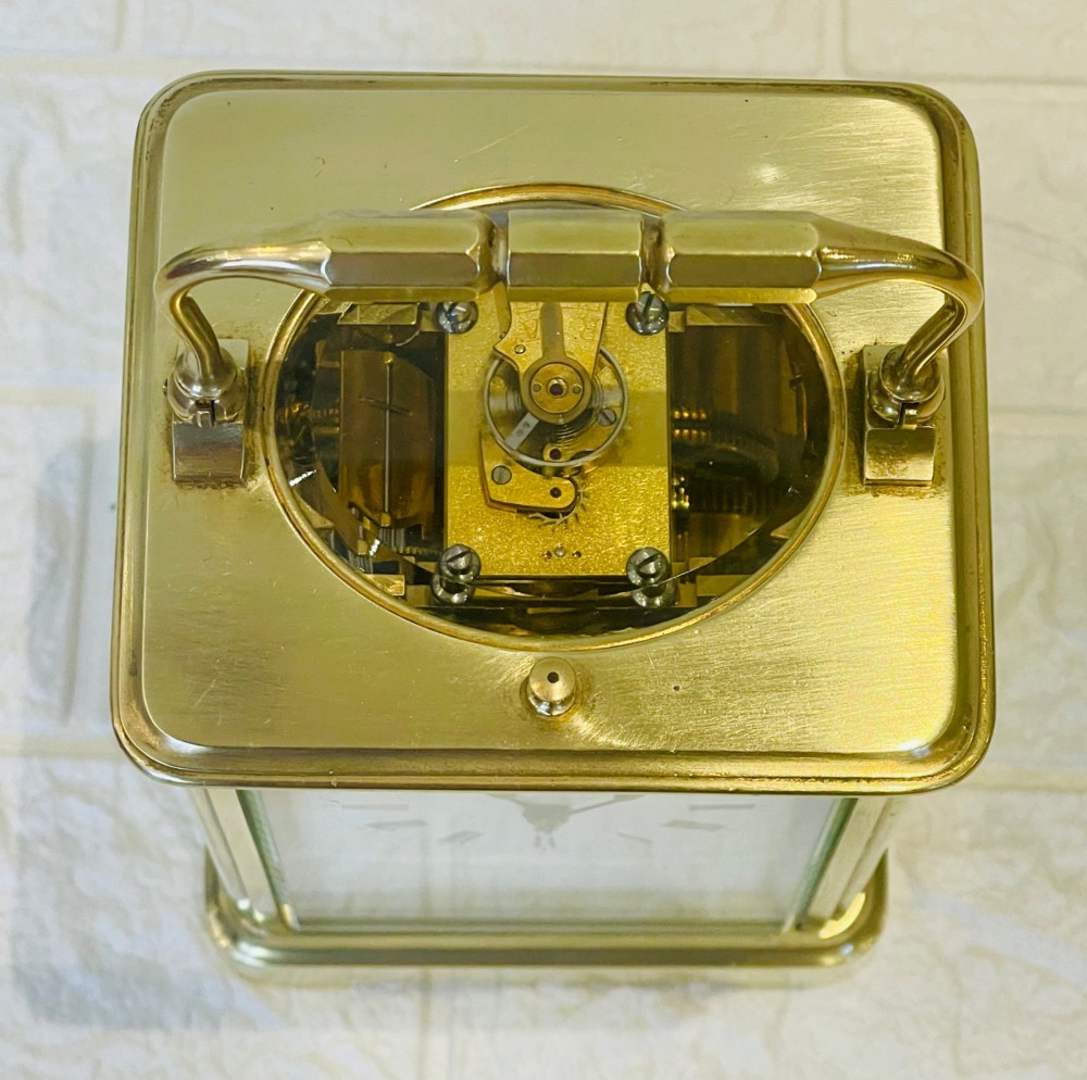 An antique brass carriage clock featuring a rectangular glass case, top carrying handle, and a white enamel dial with black Roman numerals. View II