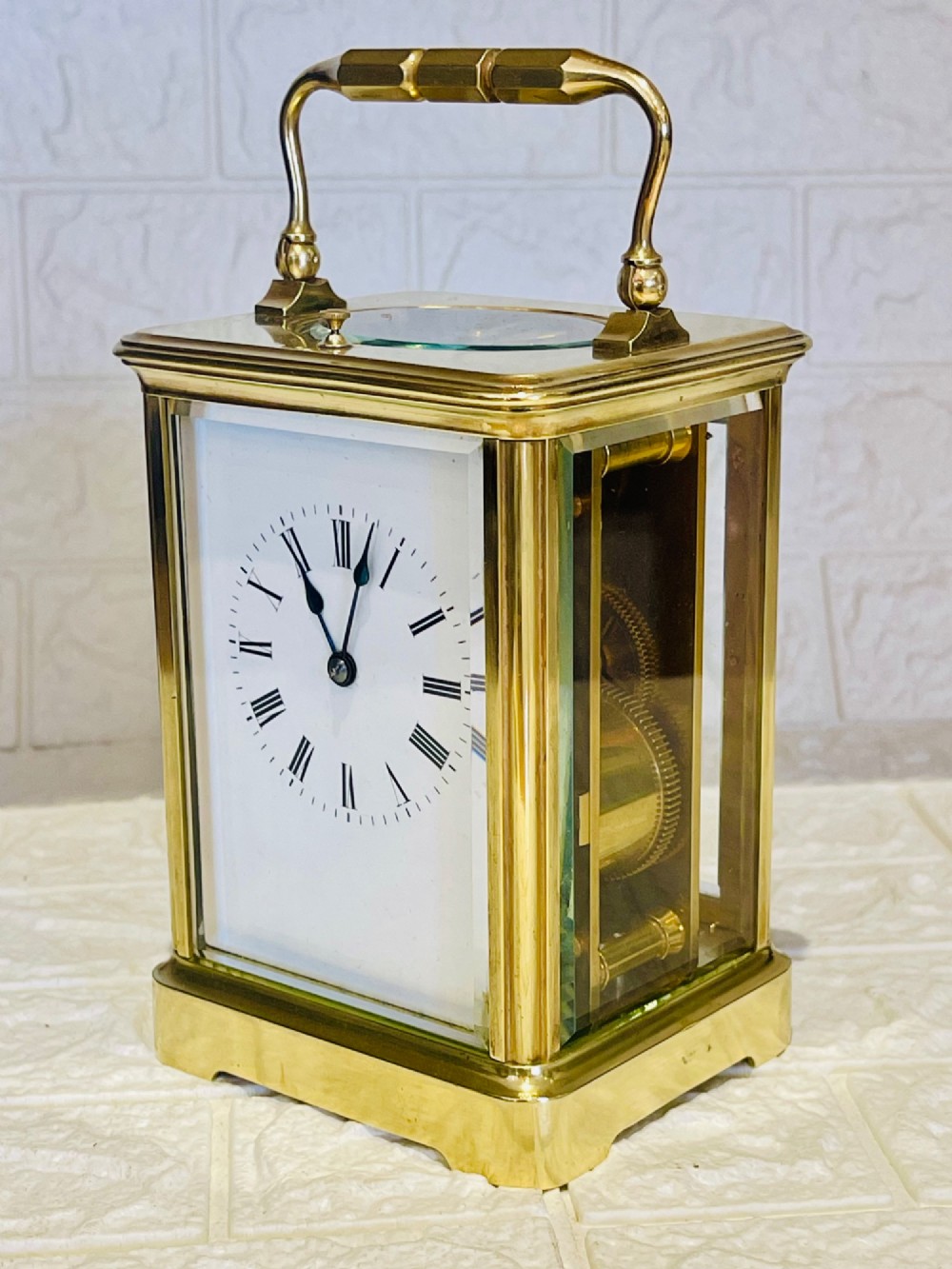 An antique brass carriage clock featuring a rectangular glass case, top carrying handle, and a white enamel dial with black Roman numerals. View III