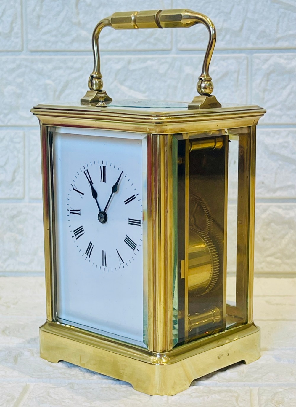 An antique brass carriage clock featuring a rectangular glass case, top carrying handle, and a white enamel dial with black Roman numerals. View V