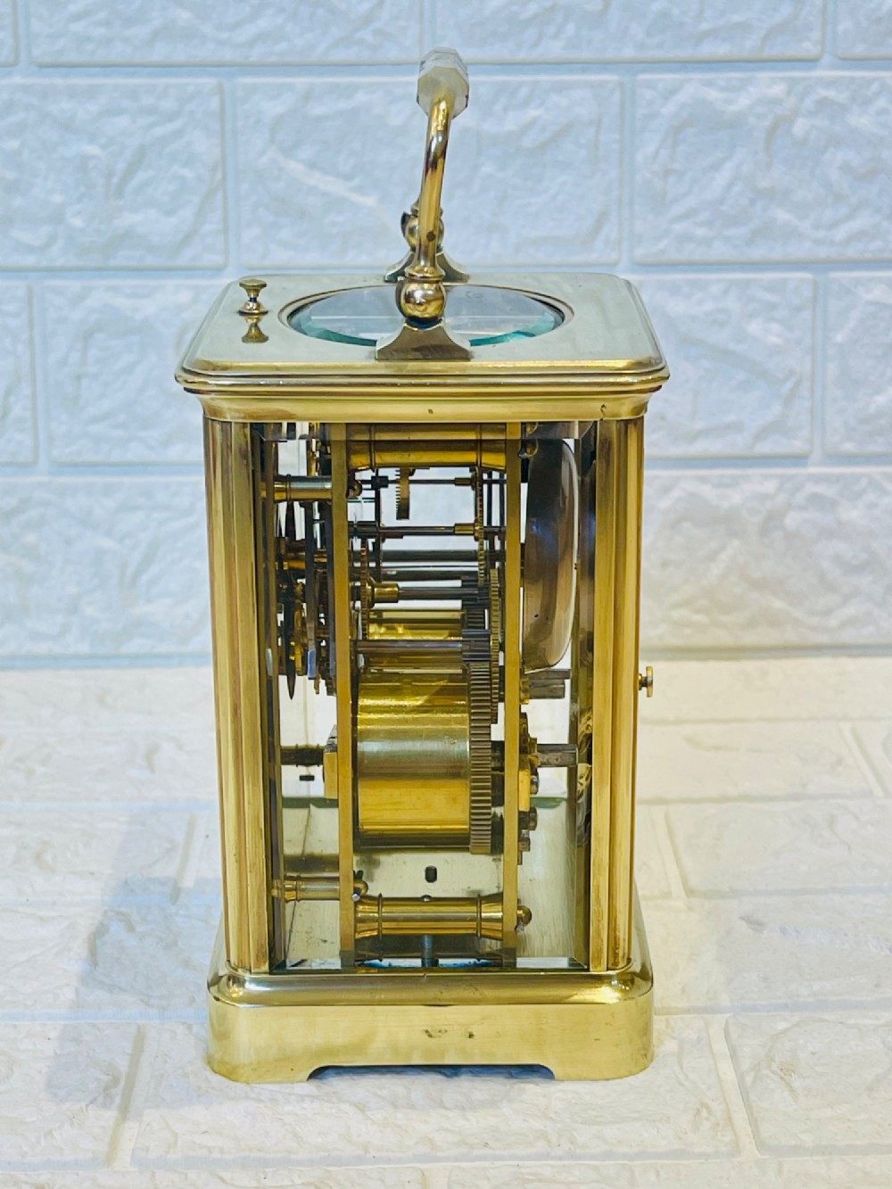 An antique brass carriage clock featuring a rectangular glass case, top carrying handle, and a white enamel dial with black Roman numerals. View VI