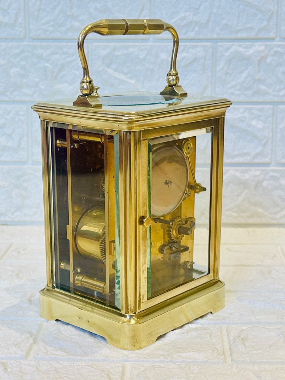 An antique brass carriage clock featuring a rectangular glass case, top carrying handle, and a white enamel dial with black Roman numerals. View VII