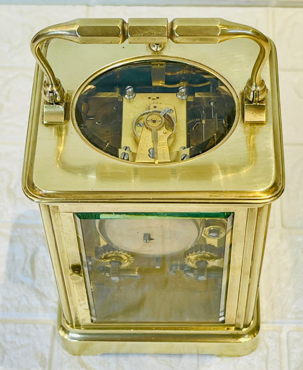 An antique brass carriage clock featuring a rectangular glass case, top carrying handle, and a white enamel dial with black Roman numerals. View IX