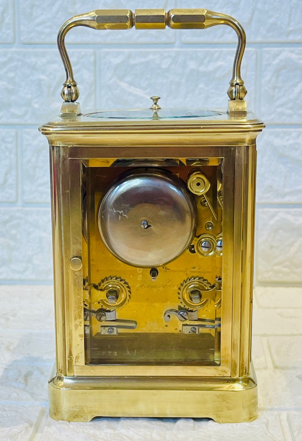 An antique brass carriage clock featuring a rectangular glass case, top carrying handle, and a white enamel dial with black Roman numerals. View X