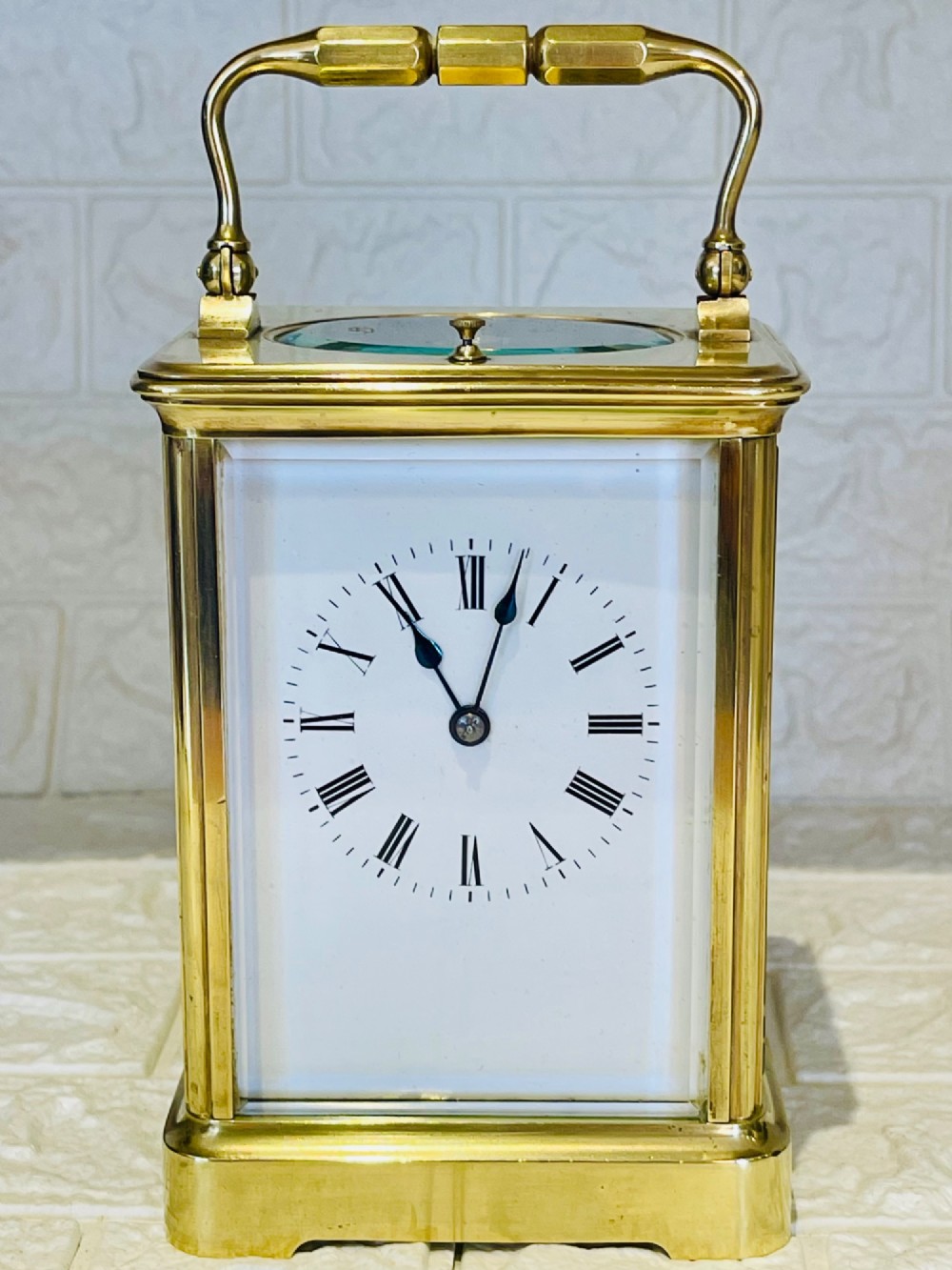 An antique brass carriage clock featuring a rectangular glass case, top carrying handle, and a white enamel dial with black Roman numerals. View XI