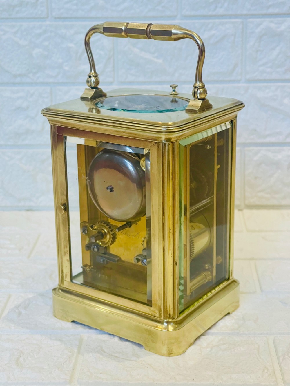 An antique brass carriage clock featuring a rectangular glass case, top carrying handle, and a white enamel dial with black Roman numerals. View XII