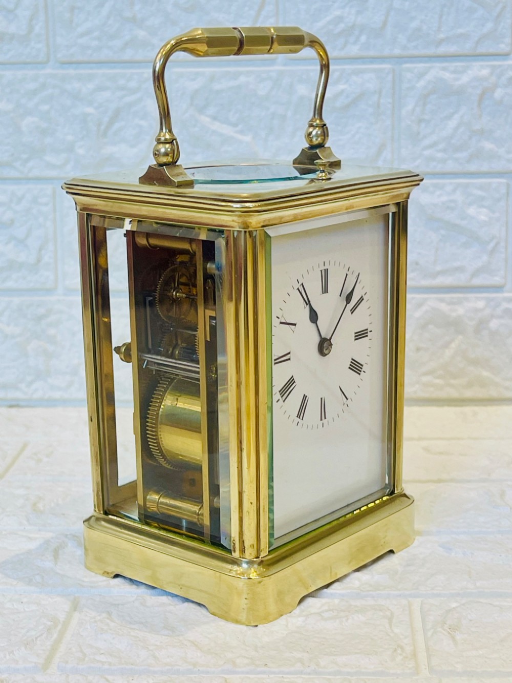 An antique brass carriage clock featuring a rectangular glass case, top carrying handle, and a white enamel dial with black Roman numerals. View XIV