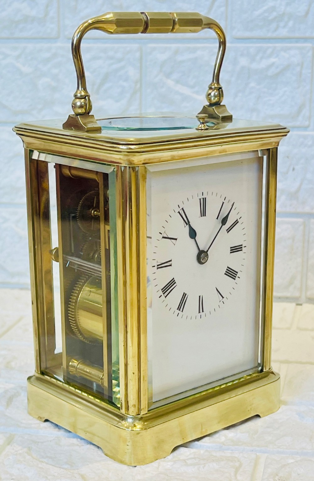 An antique brass carriage clock featuring a rectangular glass case, top carrying handle, and a white enamel dial with black Roman numerals. View XV