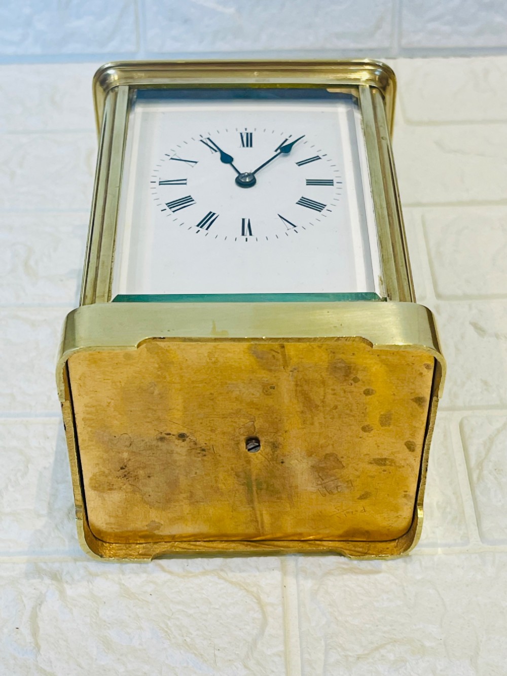 An antique brass carriage clock featuring a rectangular glass case, top carrying handle, and a white enamel dial with black Roman numerals. View XVI