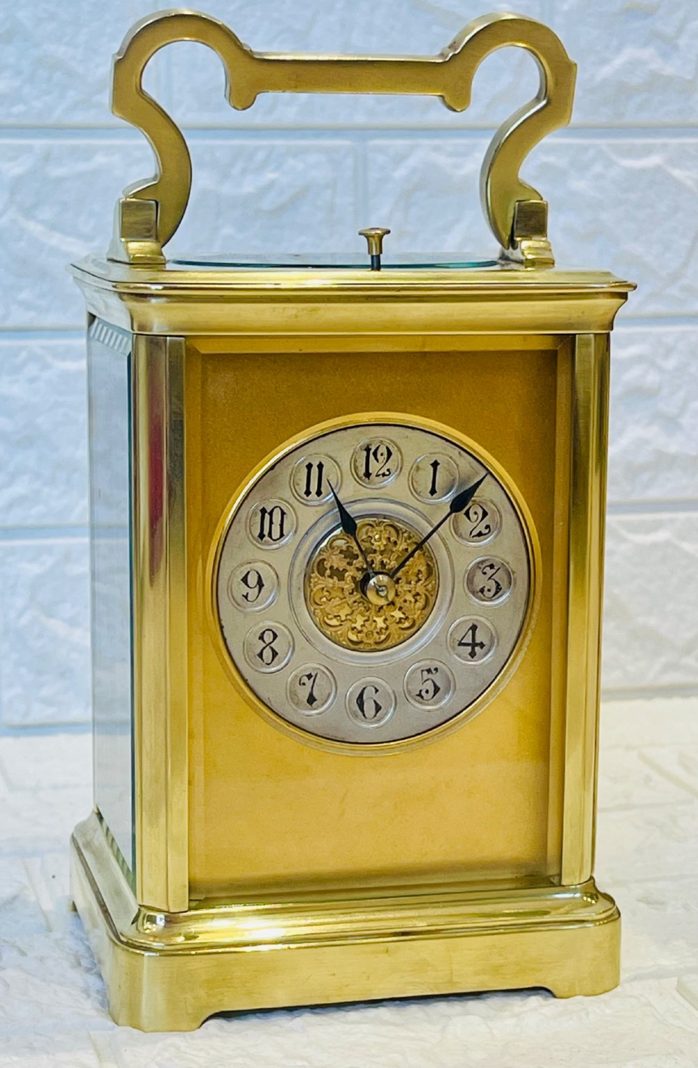 A polished brass repeating carriage clock featuring clear glass side panels, a scrolled top handle, and a silvered circular dial with Arabic numerals and a pierced gilt centre.