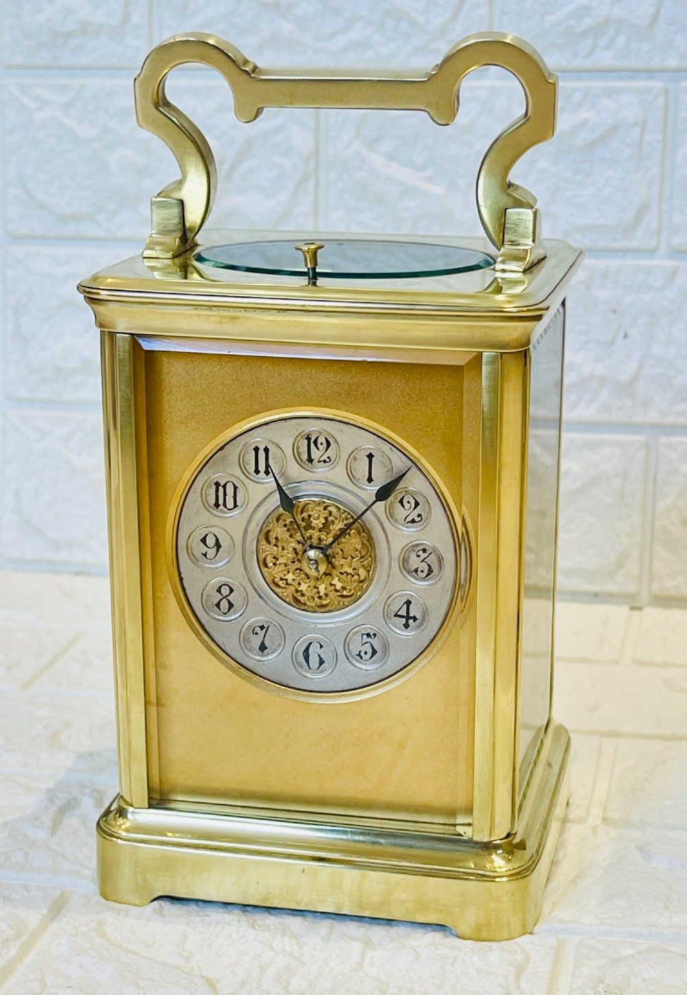 A polished brass repeating carriage clock featuring clear glass side panels, a scrolled top handle, and a silvered circular dial with Arabic numerals and a pierced gilt centre. View II