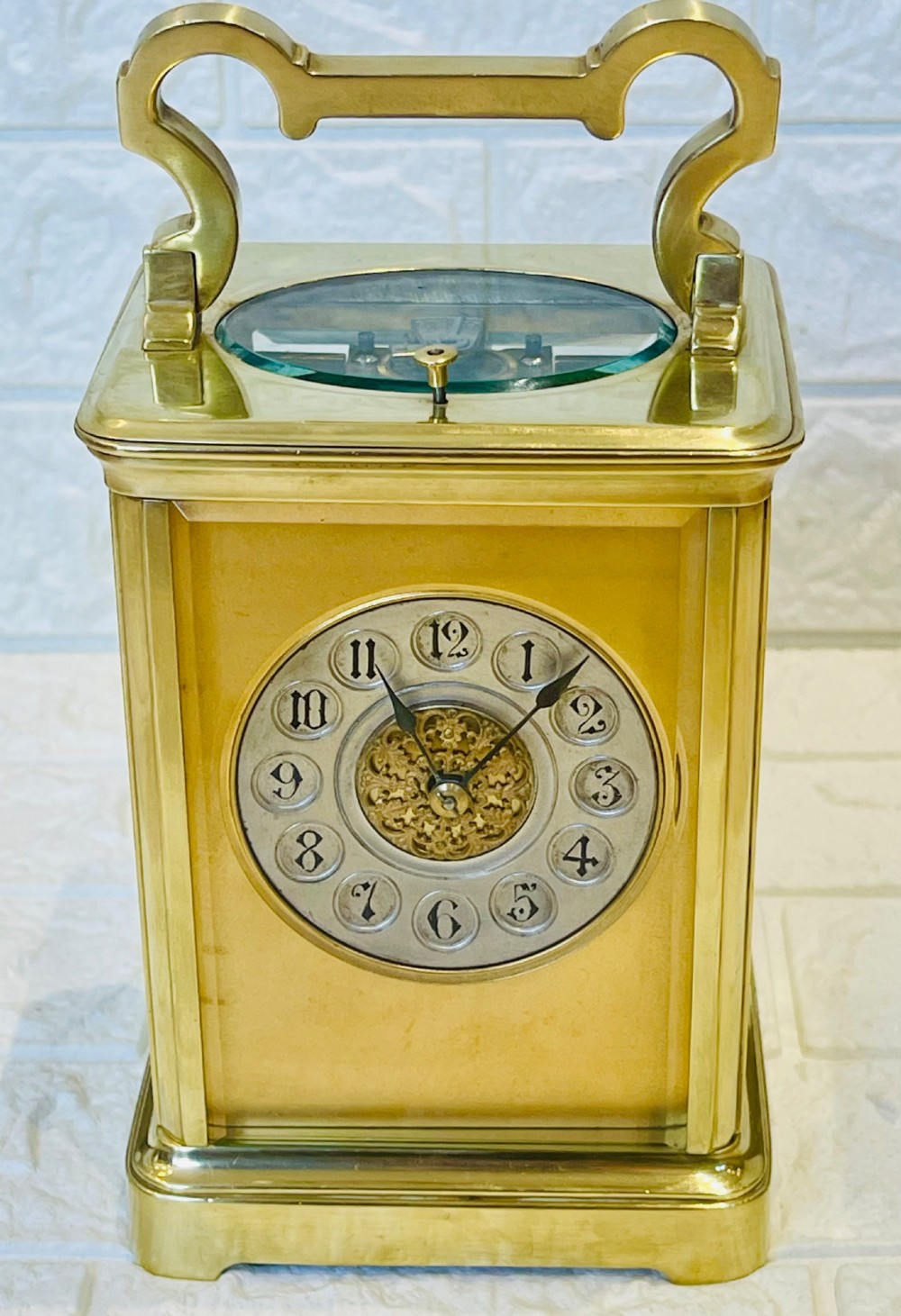 A polished brass repeating carriage clock featuring clear glass side panels, a scrolled top handle, and a silvered circular dial with Arabic numerals and a pierced gilt centre. View III