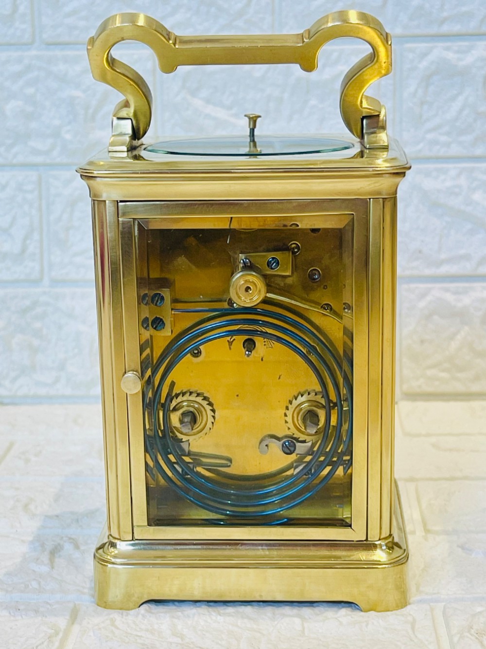 A polished brass repeating carriage clock featuring clear glass side panels, a scrolled top handle, and a silvered circular dial with Arabic numerals and a pierced gilt centre. View VI