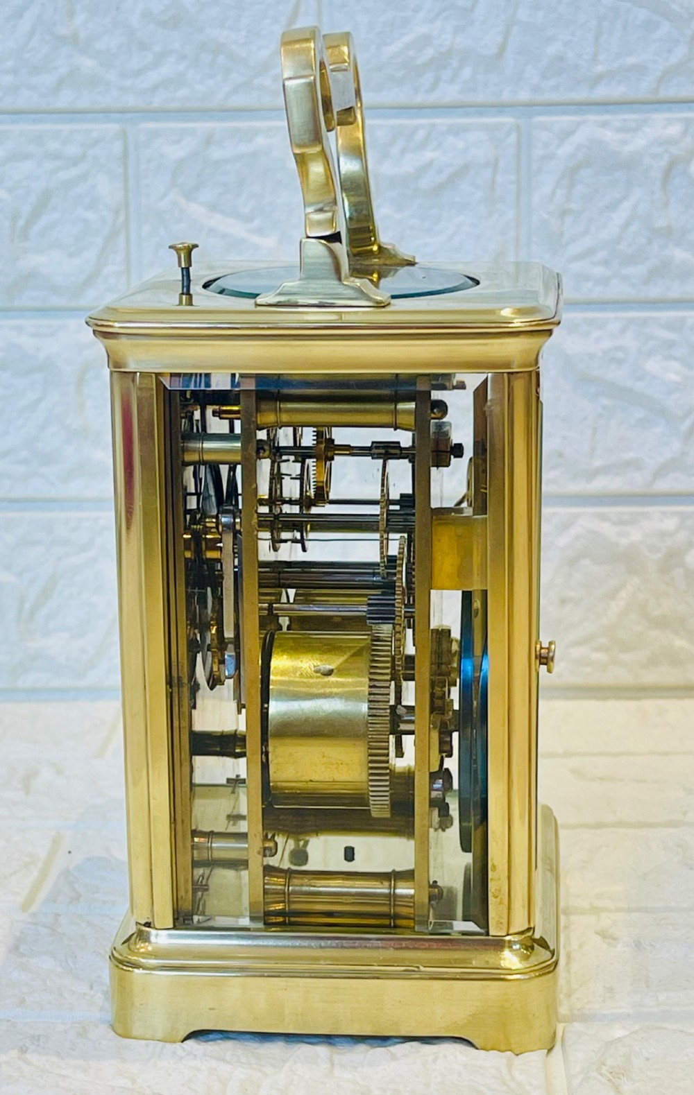 A polished brass repeating carriage clock featuring clear glass side panels, a scrolled top handle, and a silvered circular dial with Arabic numerals and a pierced gilt centre. View VIII