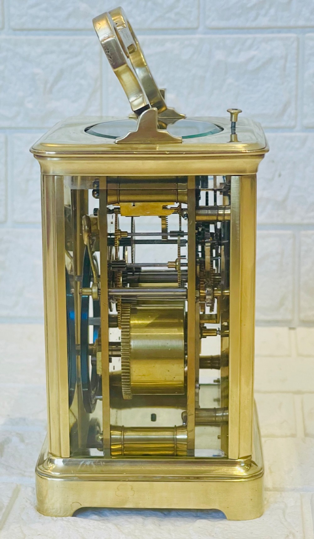 A polished brass repeating carriage clock featuring clear glass side panels, a scrolled top handle, and a silvered circular dial with Arabic numerals and a pierced gilt centre. View IX