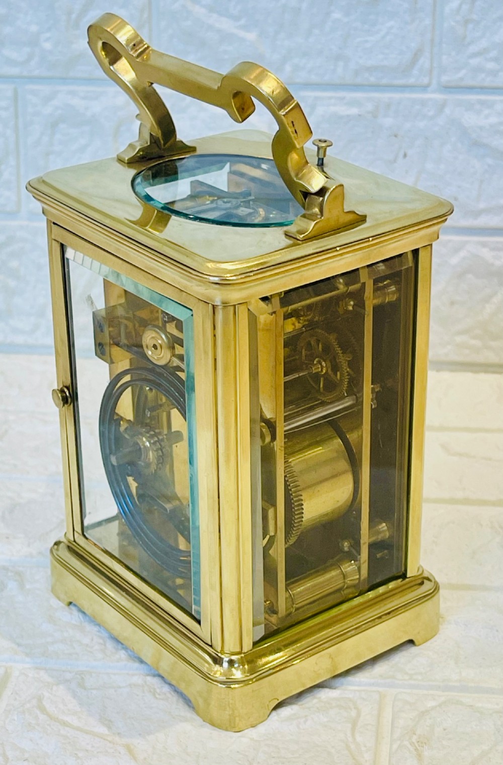A polished brass repeating carriage clock featuring clear glass side panels, a scrolled top handle, and a silvered circular dial with Arabic numerals and a pierced gilt centre. View X