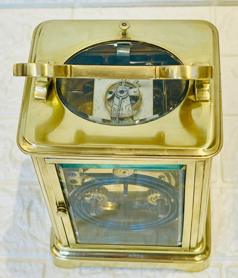 A polished brass repeating carriage clock featuring clear glass side panels, a scrolled top handle, and a silvered circular dial with Arabic numerals and a pierced gilt centre. View XI