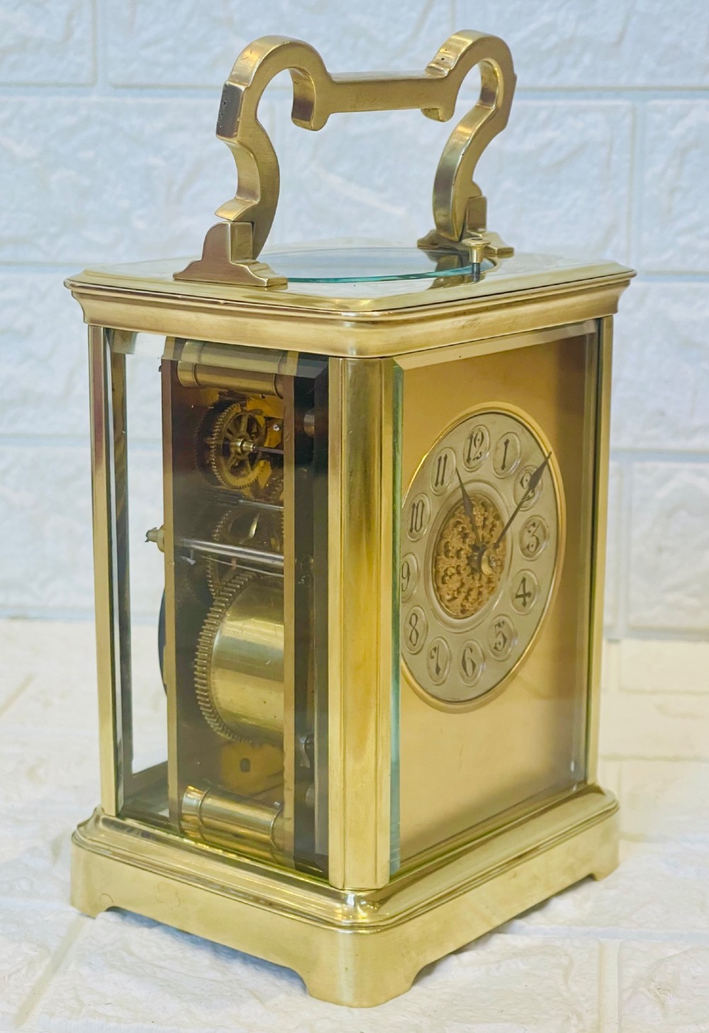 A polished brass repeating carriage clock featuring clear glass side panels, a scrolled top handle, and a silvered circular dial with Arabic numerals and a pierced gilt centre. View XIII