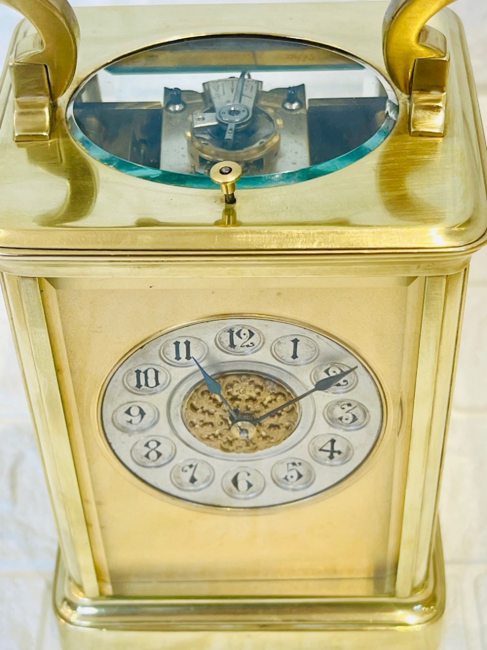 A polished brass repeating carriage clock featuring clear glass side panels, a scrolled top handle, and a silvered circular dial with Arabic numerals and a pierced gilt centre. View XIV