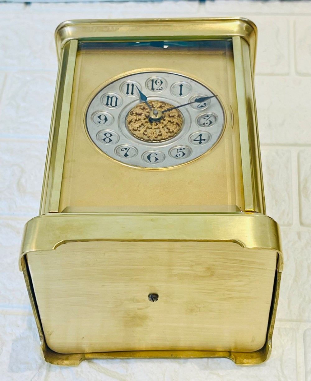 A polished brass repeating carriage clock featuring clear glass side panels, a scrolled top handle, and a silvered circular dial with Arabic numerals and a pierced gilt centre. View XV