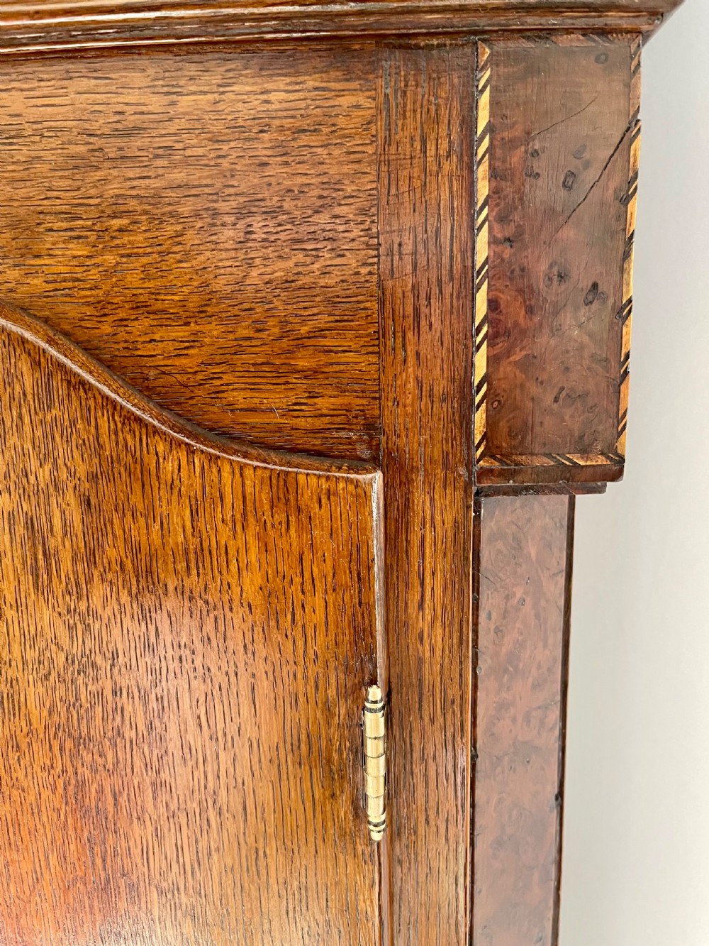 An antique Georgian longcase clock featuring a walnut and oak case, swan-neck pediment, brass finial, and an engraved brass dial with a moonphase display. View XII