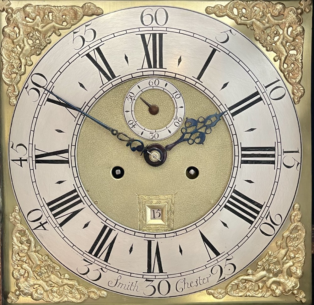 An 18th-century Georgian oak longcase clock featuring a square brass dial with silvered chapter ring, brass spandrels, twin brass finials, and a tall slender timber case. View II