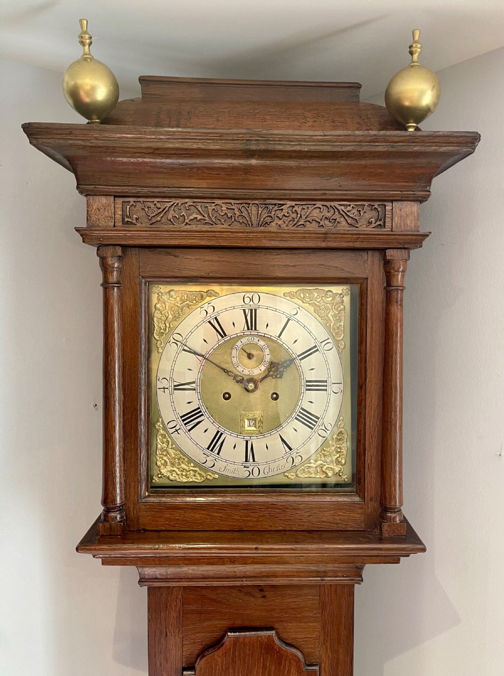 An 18th-century Georgian oak longcase clock featuring a square brass dial with silvered chapter ring, brass spandrels, twin brass finials, and a tall slender timber case. View III