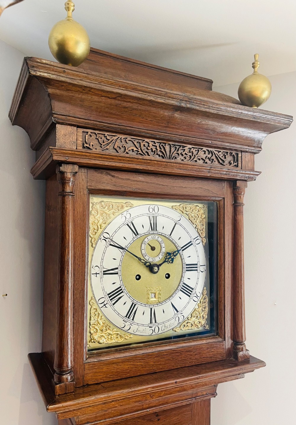 An 18th-century Georgian oak longcase clock featuring a square brass dial with silvered chapter ring, brass spandrels, twin brass finials, and a tall slender timber case. View IV