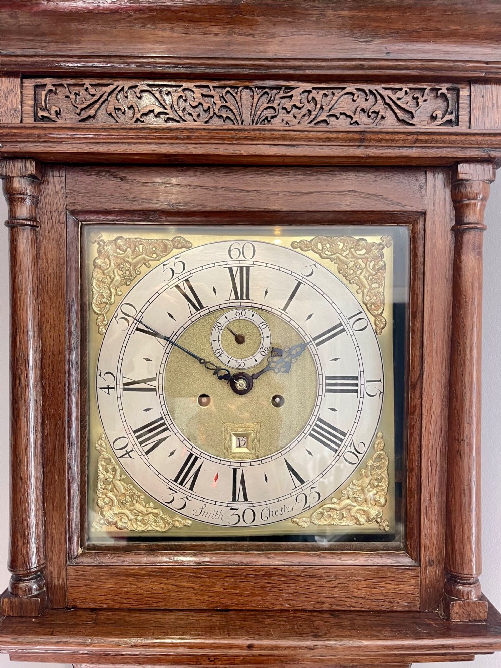 An 18th-century Georgian oak longcase clock featuring a square brass dial with silvered chapter ring, brass spandrels, twin brass finials, and a tall slender timber case. View VI