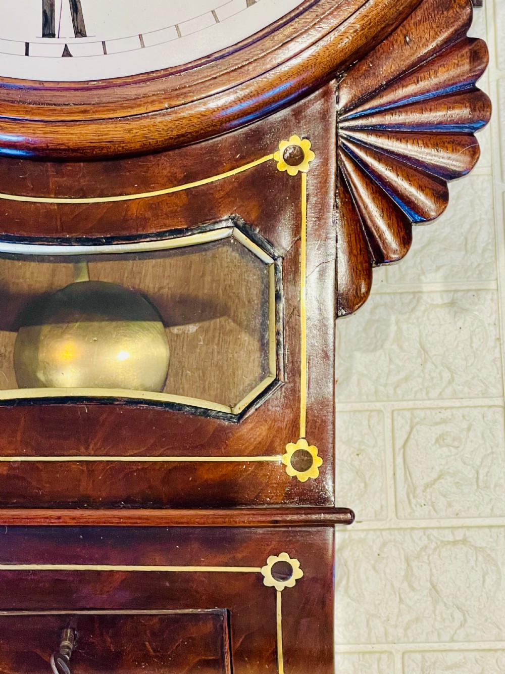 An antique Regency mahogany drop dial wall clock featuring brass line inlay, carved fan side ears, and a cream dial with Roman numerals. View XIII