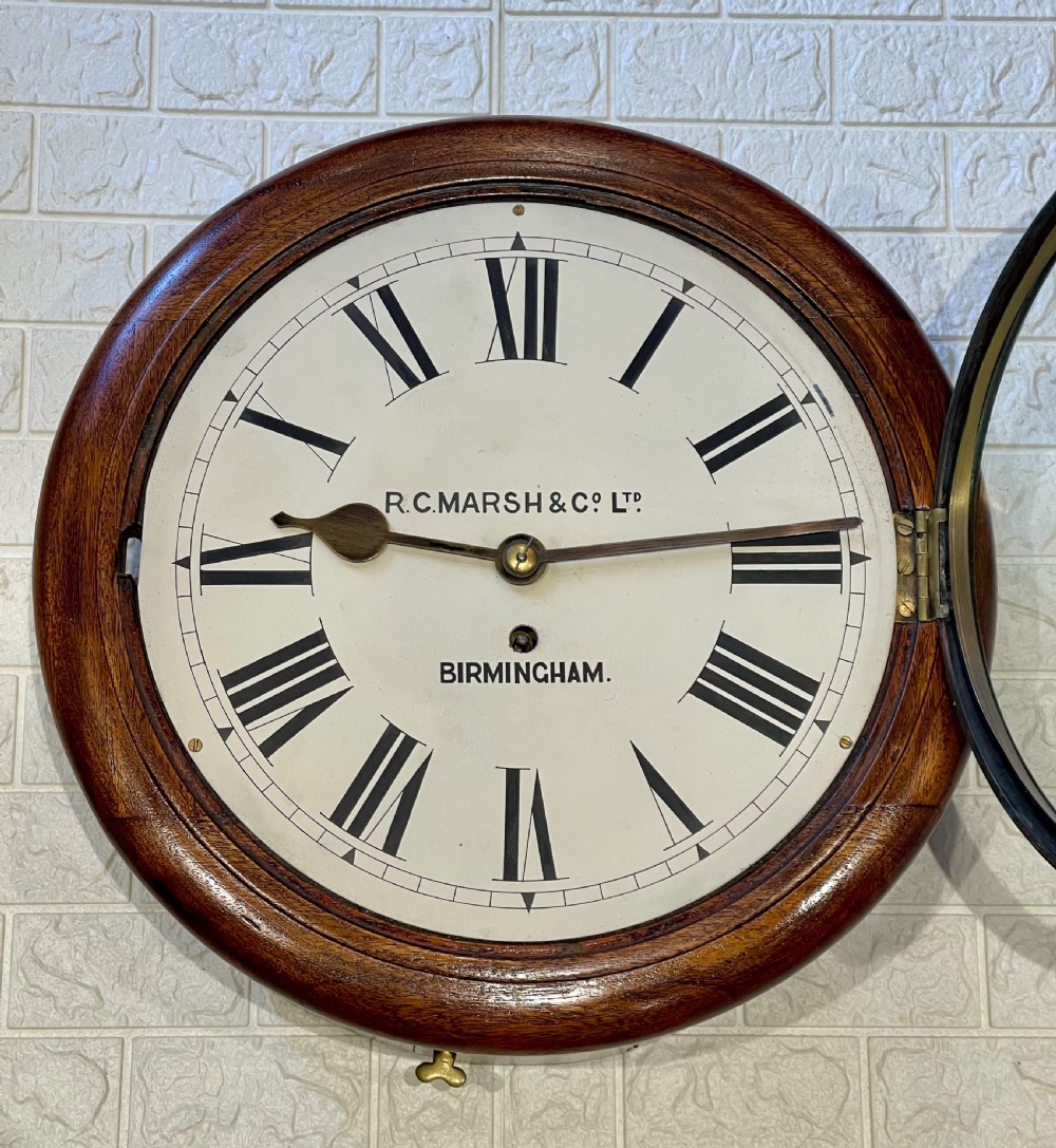 A circular Victorian oak fusee wall clock featuring a white dial with Roman numerals, black hands, and a brass bezel. View V