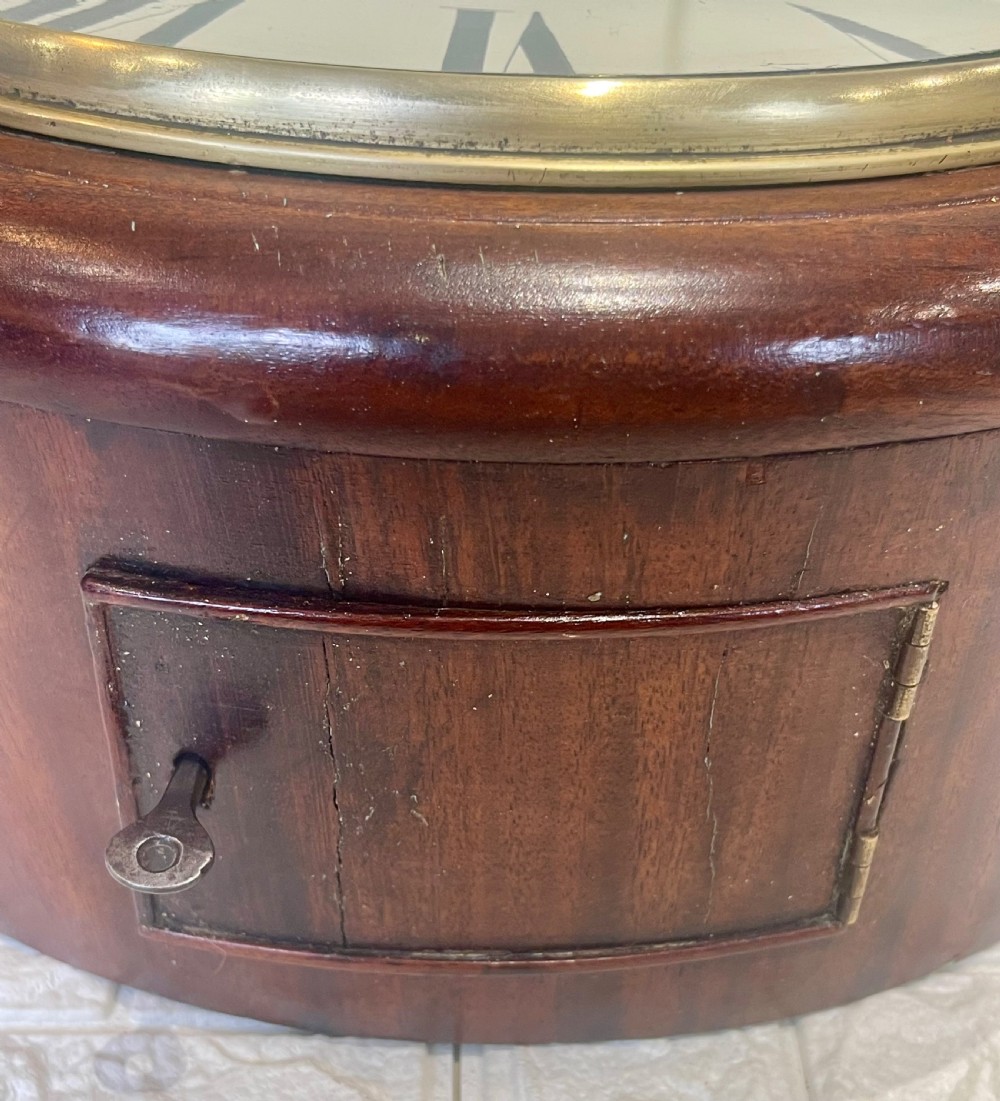 A circular Victorian oak wall clock featuring a cream painted dial with Roman numerals, black hands, a brass bezel, and the maker inscription Butcher, Wellingborough. View VII
