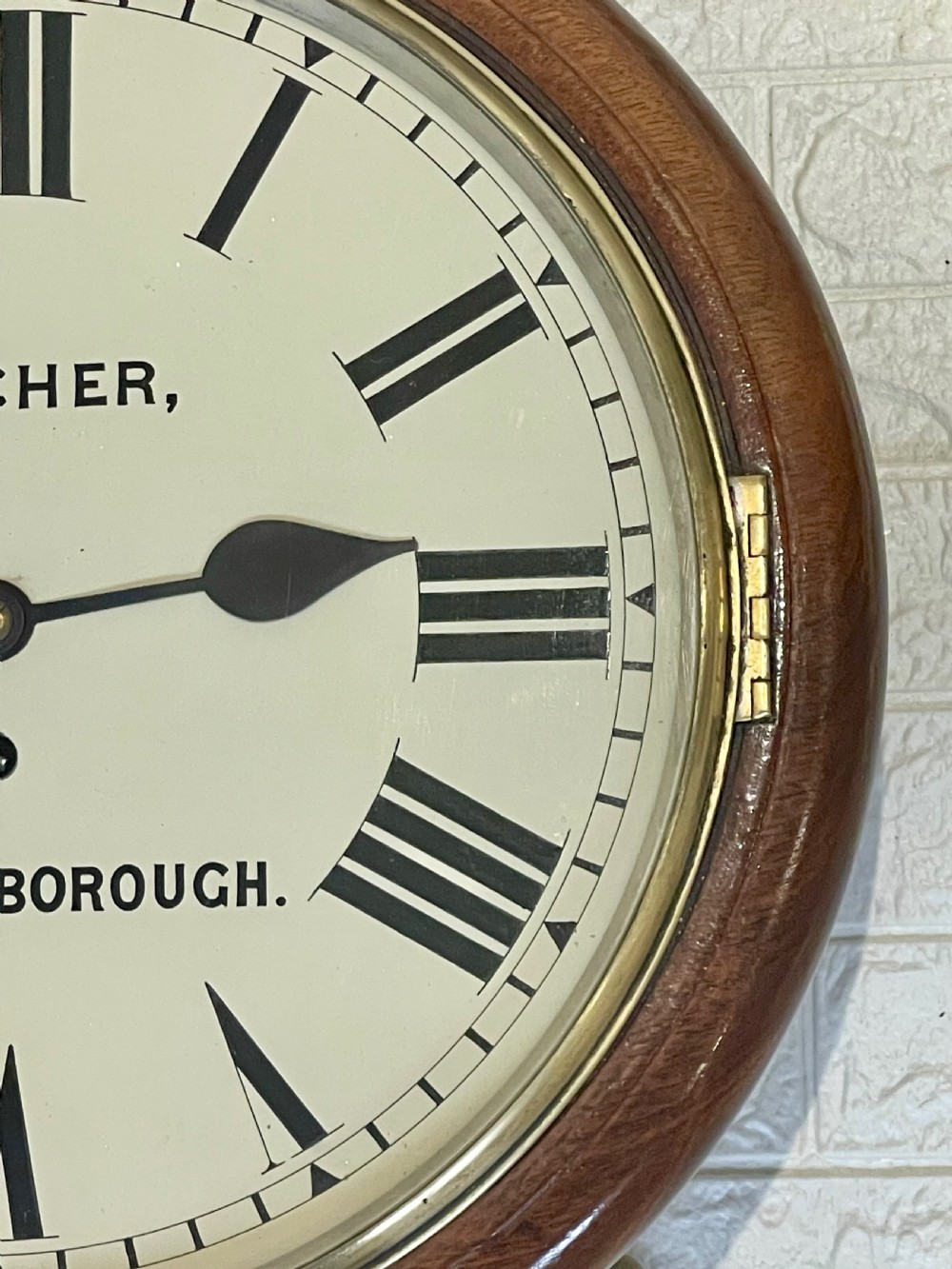 A circular Victorian oak wall clock featuring a cream painted dial with Roman numerals, black hands, a brass bezel, and the maker inscription Butcher, Wellingborough. View XIV