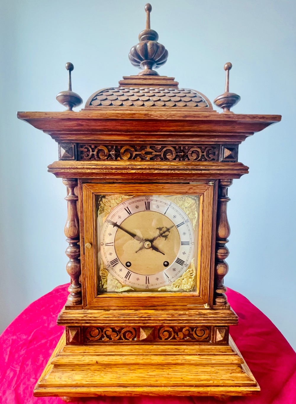 An antique carved oak bracket clock featuring finials, turned columns, and a brass dial with silvered chapter ring.