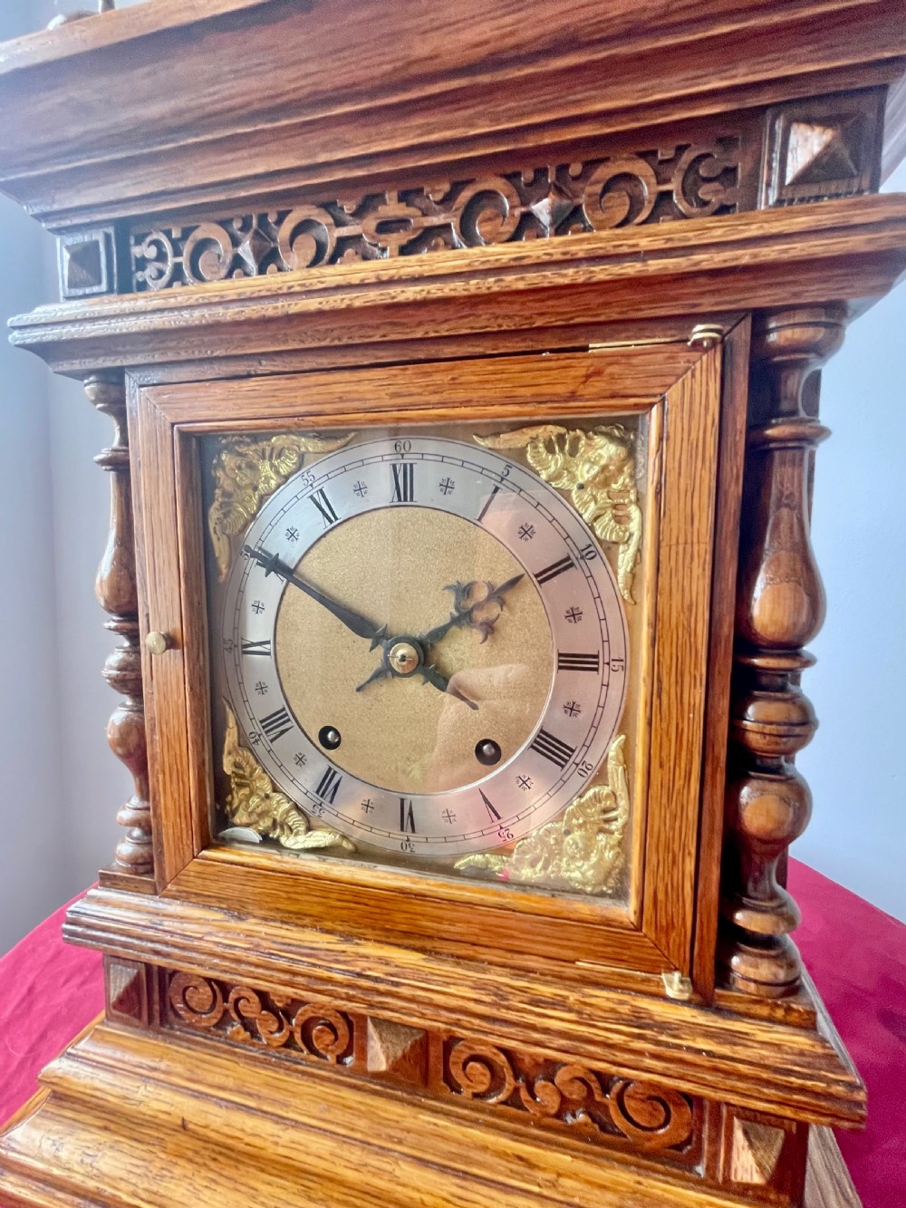 An antique carved oak bracket clock featuring finials, turned columns, and a brass dial with silvered chapter ring. View VI