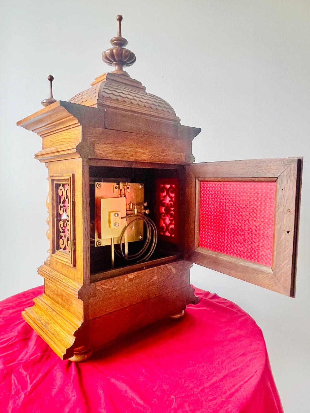 An antique carved oak bracket clock featuring finials, turned columns, and a brass dial with silvered chapter ring. View VII
