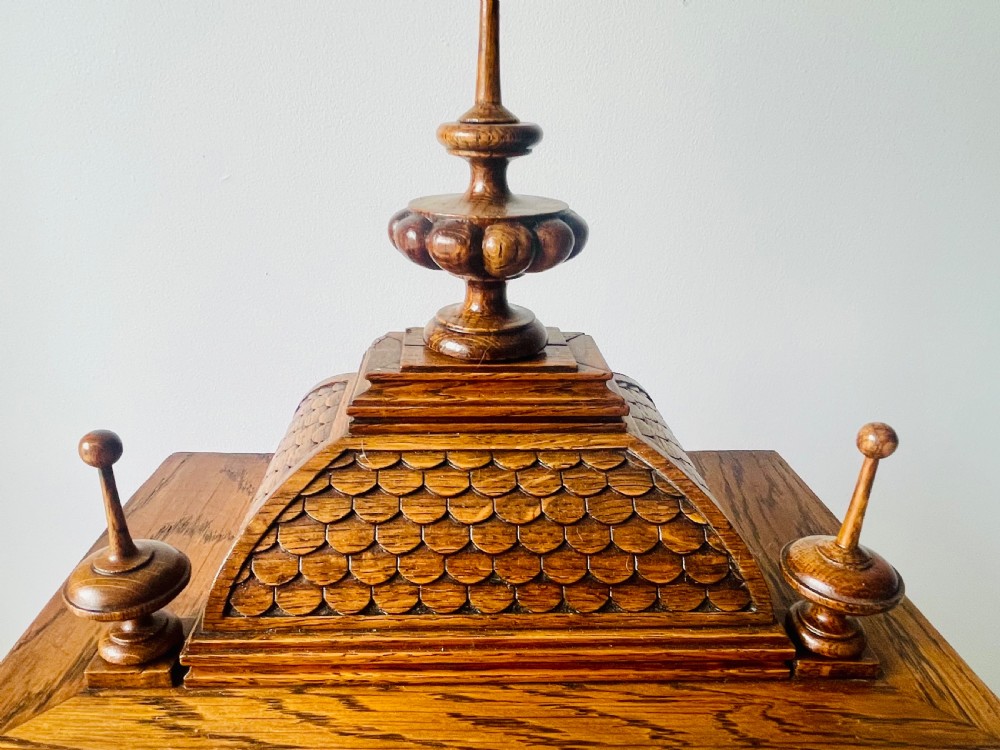 An antique carved oak bracket clock featuring finials, turned columns, and a brass dial with silvered chapter ring. View XII