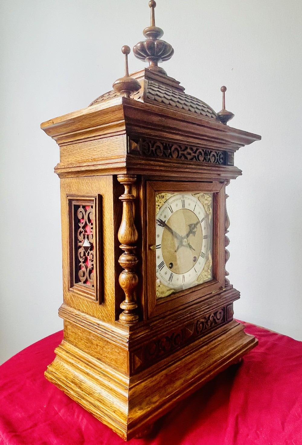 An antique carved oak bracket clock featuring finials, turned columns, and a brass dial with silvered chapter ring. View XIV