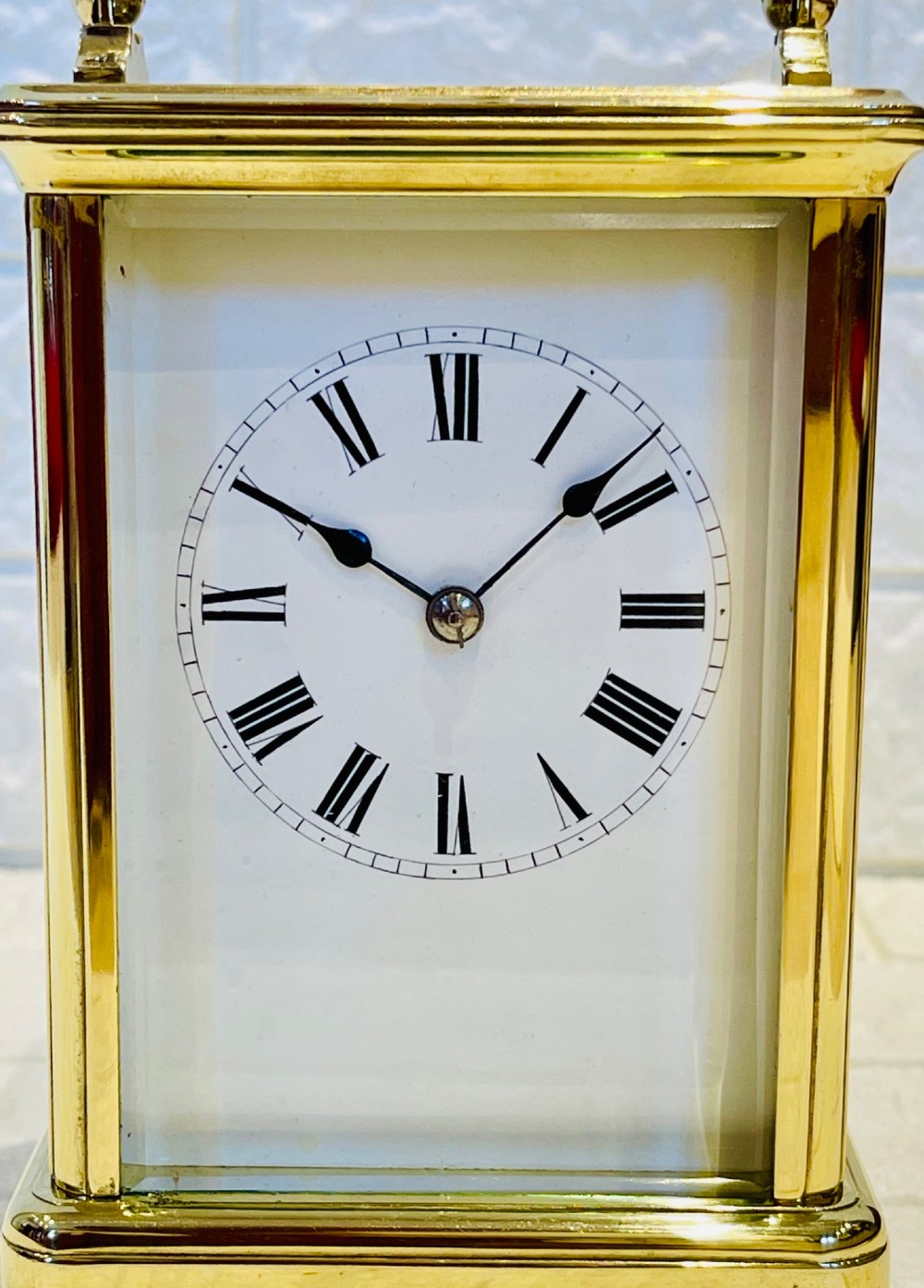 A rectangular French brass carriage clock featuring bevelled glass panels, a top carrying handle, an oval glass escapement window, and a white dial with Roman numerals. View II