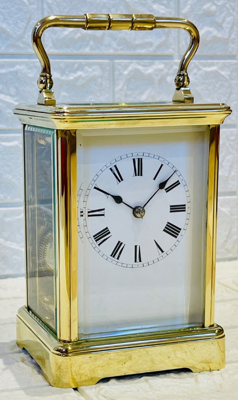 A rectangular French brass carriage clock featuring bevelled glass panels, a top carrying handle, an oval glass escapement window, and a white dial with Roman numerals. View III