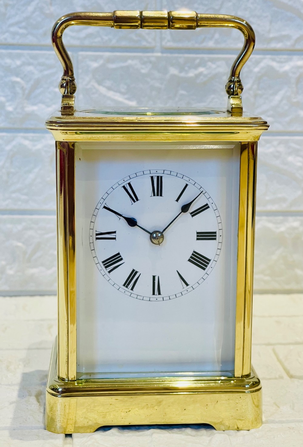 A rectangular French brass carriage clock featuring bevelled glass panels, a top carrying handle, an oval glass escapement window, and a white dial with Roman numerals. View IV