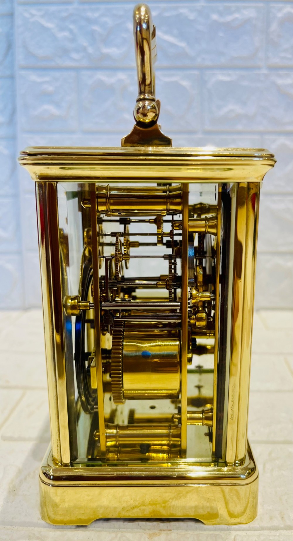 A rectangular French brass carriage clock featuring bevelled glass panels, a top carrying handle, an oval glass escapement window, and a white dial with Roman numerals. View VI