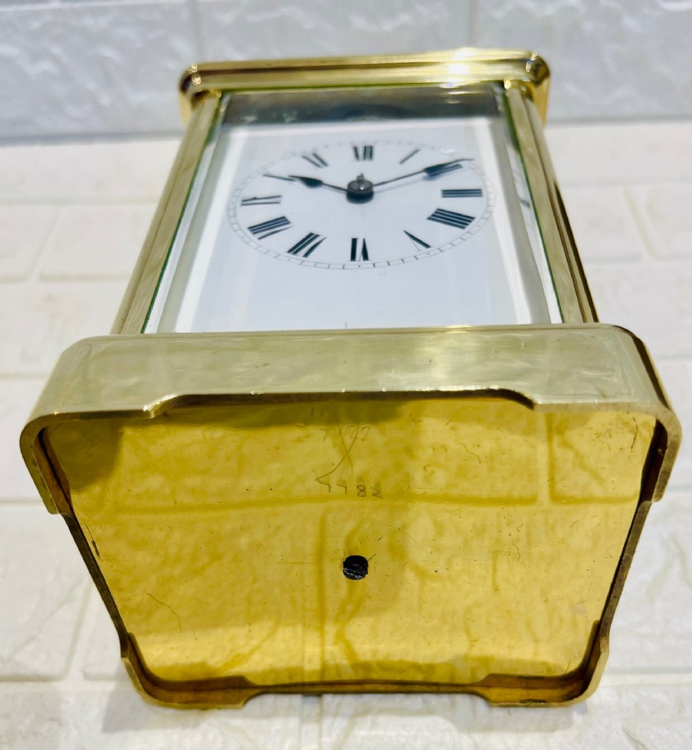 A rectangular French brass carriage clock featuring bevelled glass panels, a top carrying handle, an oval glass escapement window, and a white dial with Roman numerals. View VII